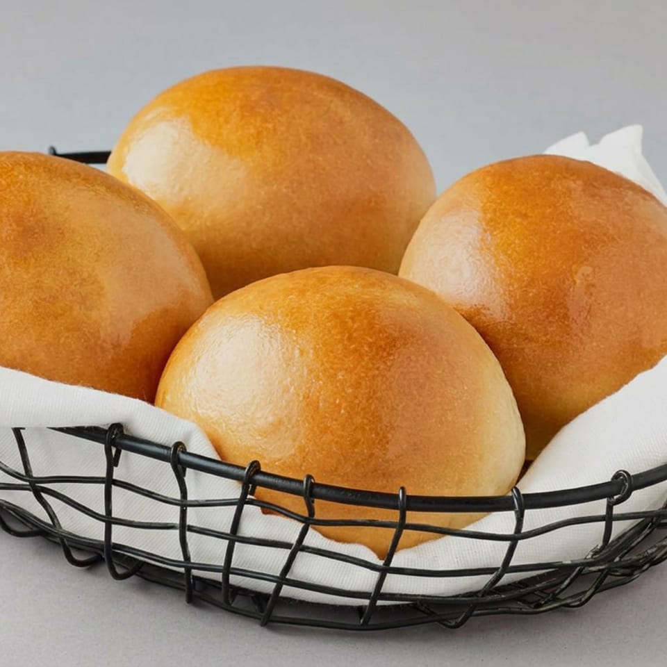 Four golden-brown bread rolls arranged in a black wire basket lined with a white napkin.