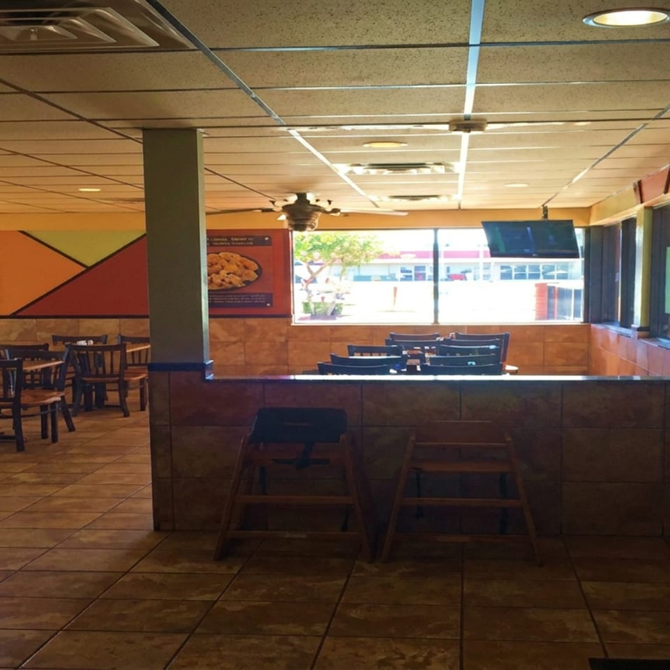 Empty casual restaurant dining area with wooden tables, chairs, colorful walls, tiled floors, and large sunlit windows.