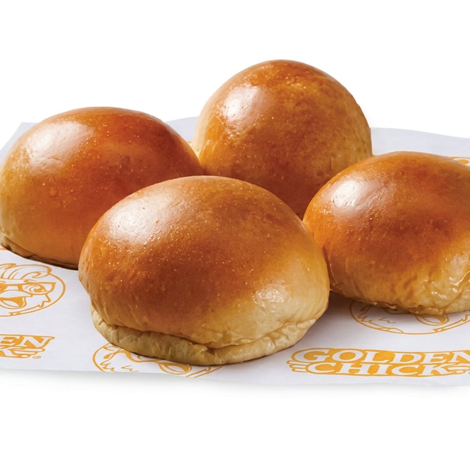 Four glossy golden-brown burger buns arranged on branded Golden Chick paper against a white background.